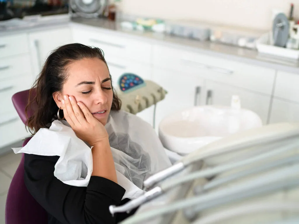 a woman sits in a dentist chair holding her jaw