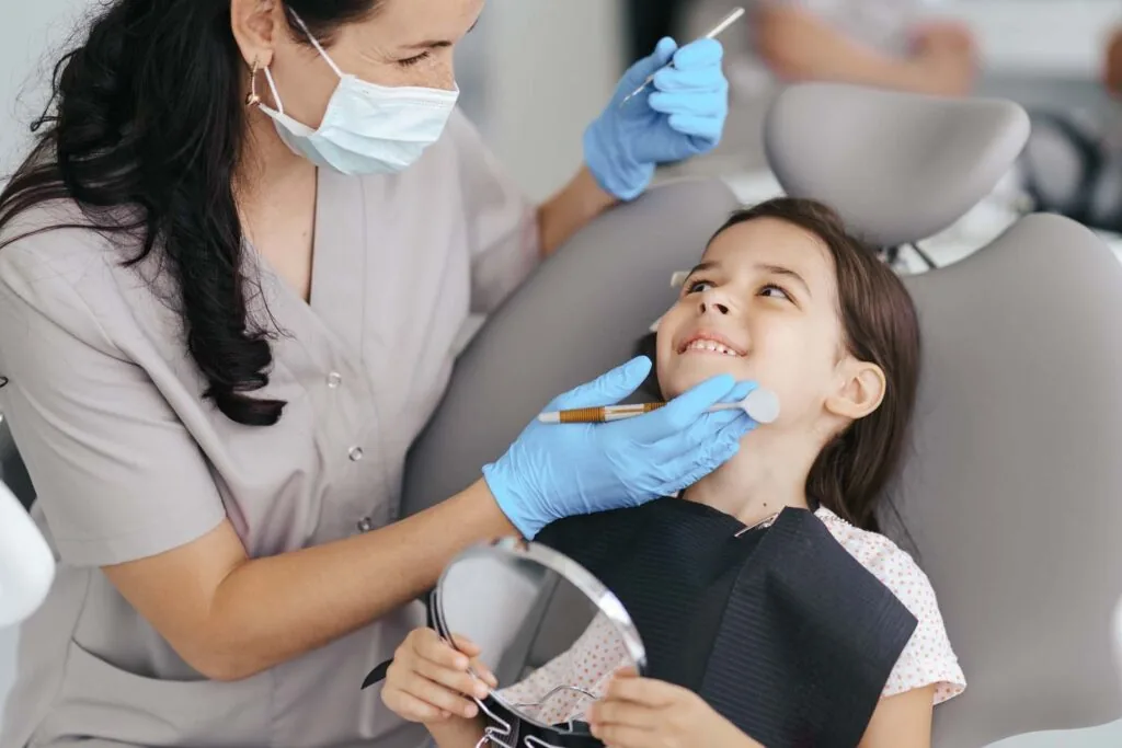 Little girl sitting on a modern dental chair and having dental consultation with dentist